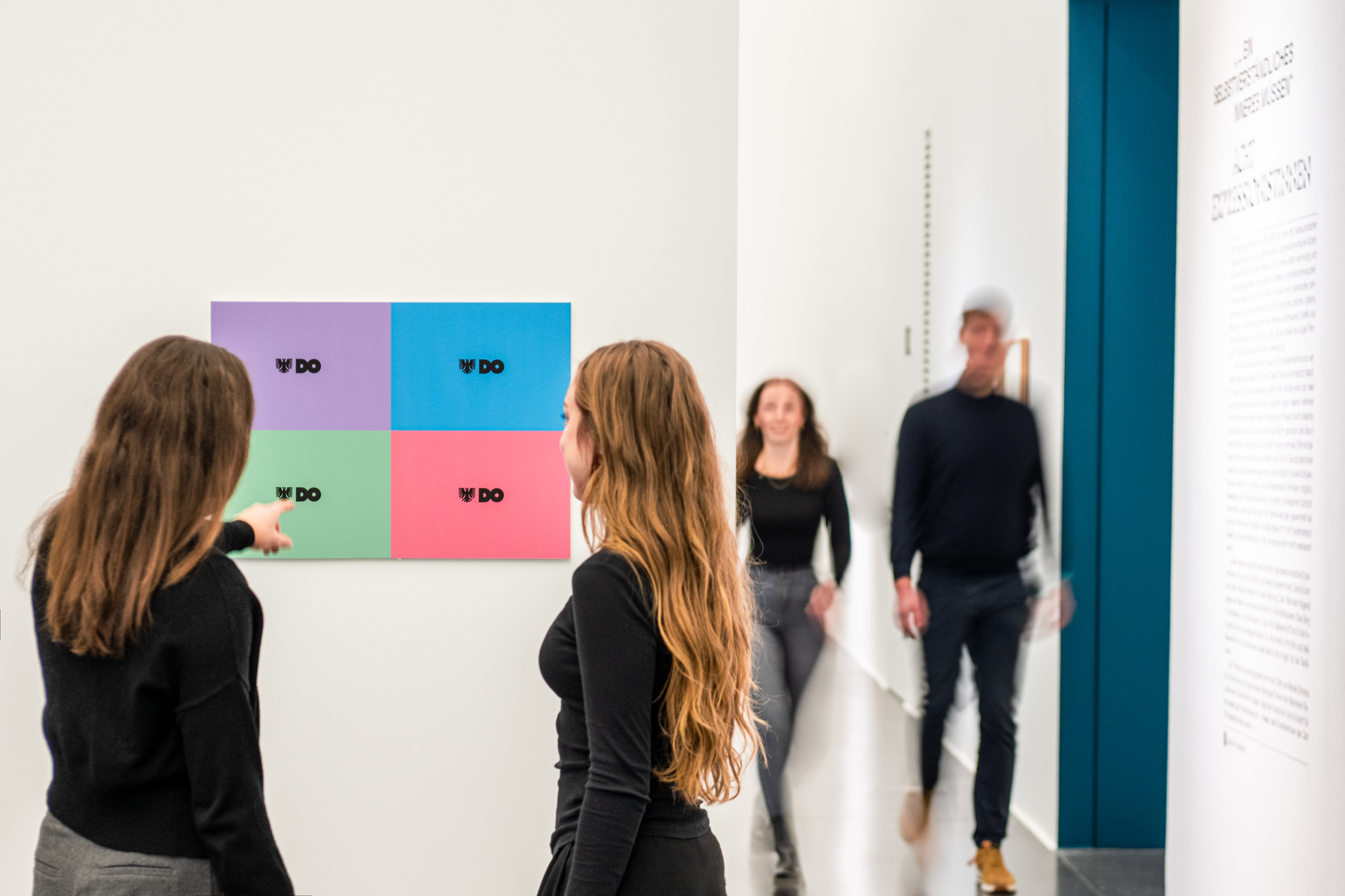 Mehrere Personen, die durch weiße Ausstellungsräume gehen. Im Vordergrund zwei Menschen, die auf die neuen Stadtfarben von Dortmund schauen. 