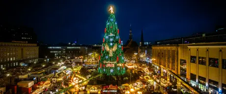 Der hell erleuchtete Weihnachtsbaum in der Weihnachtsstadt Dortmund. An seinem Fuß sind die erleuchteten Stände.