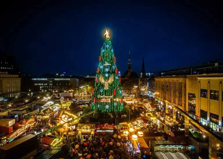 Der hell erleuchtete Weihnachtsbaum in der Weihnachtsstadt Dortmund. An seinem Fuß sind die erleuchteten Stände.