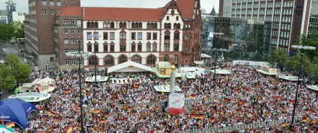 Zahlreiche Fußballfans mit Deutschlandflaggen feiern auf dem Friedensplatz.