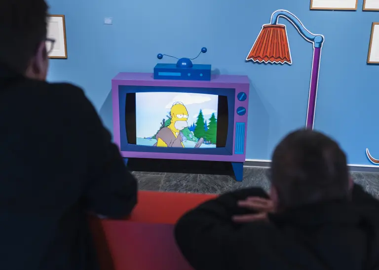 Zwei unscharfe Personen im Vordergrund schauen auf den Simpsons-Fernseher.