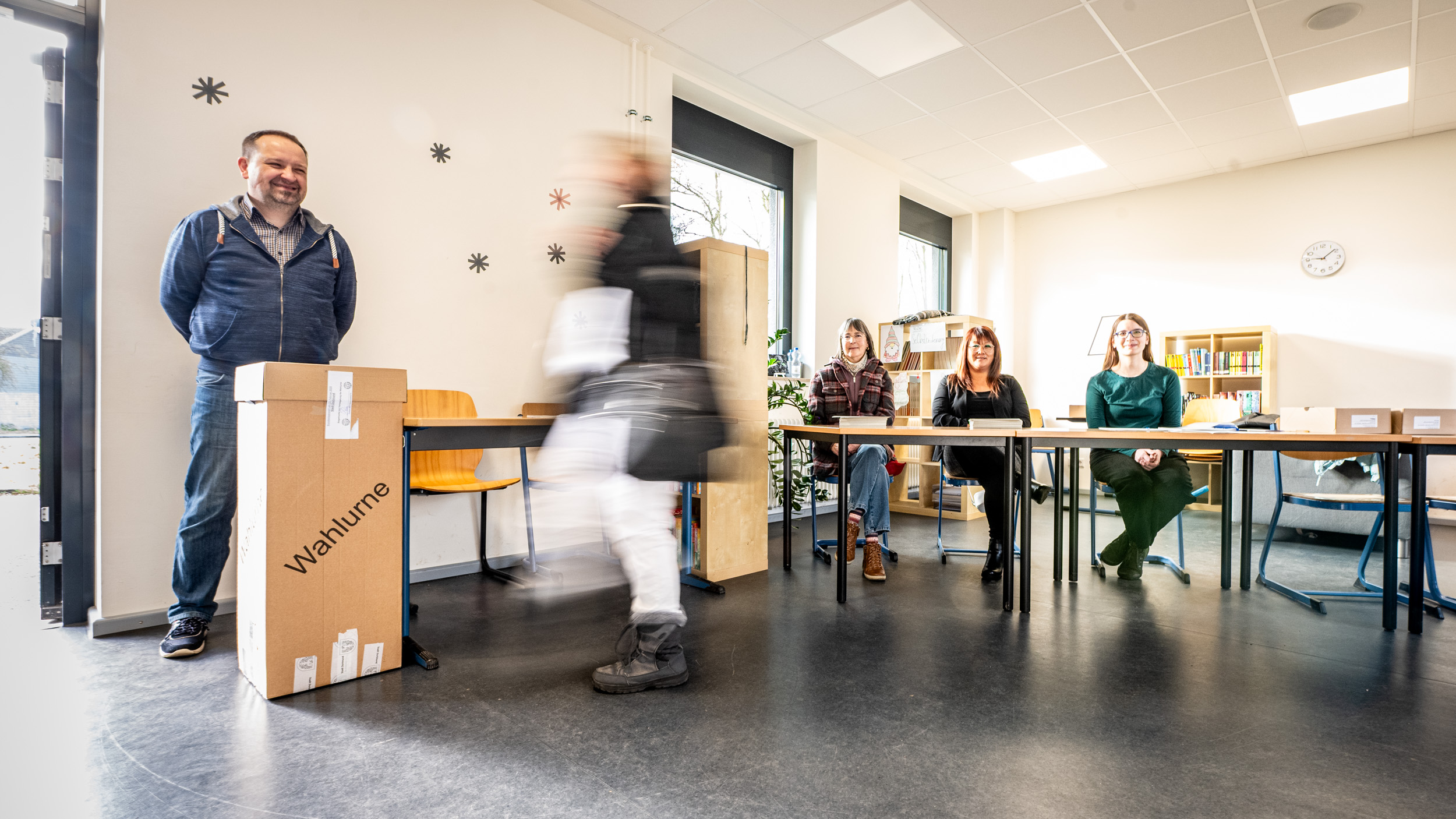 Eine Person in einem Wahllokal geht auf die Wahlurne zu.