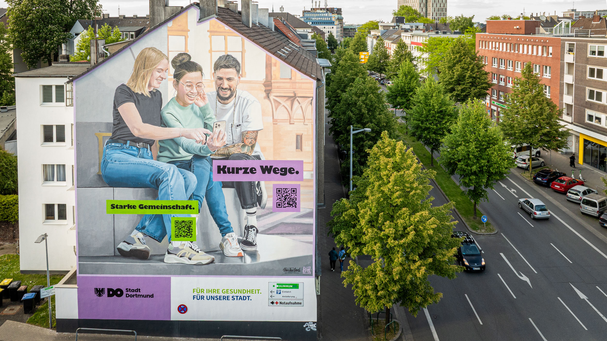 Wandbild am Klinik-Parkhaus Dortmund zeigt drei junge Menschen, die gemeinsam auf ein Handy schauen