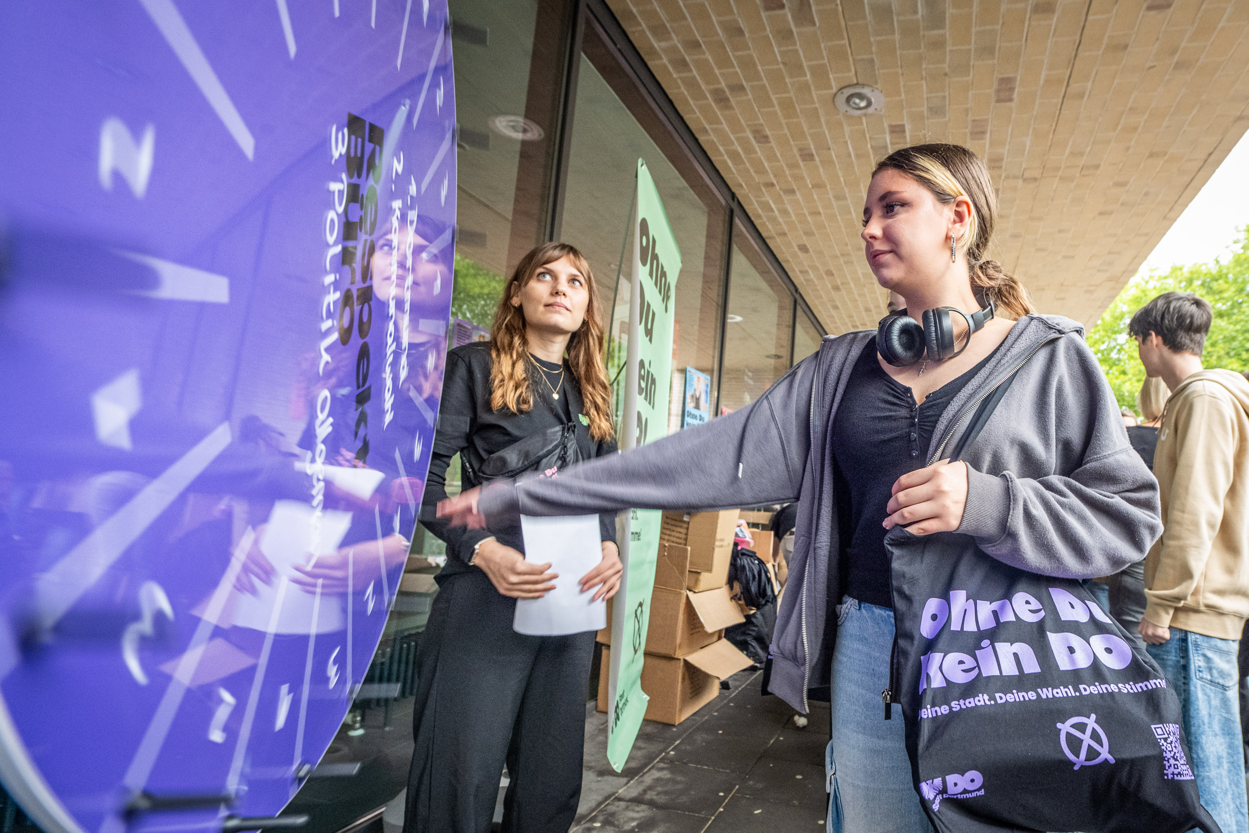 Eine Schülerin mit einem "ohne du kein do" beutel über der Schulter dreht an einem Glücksrad.