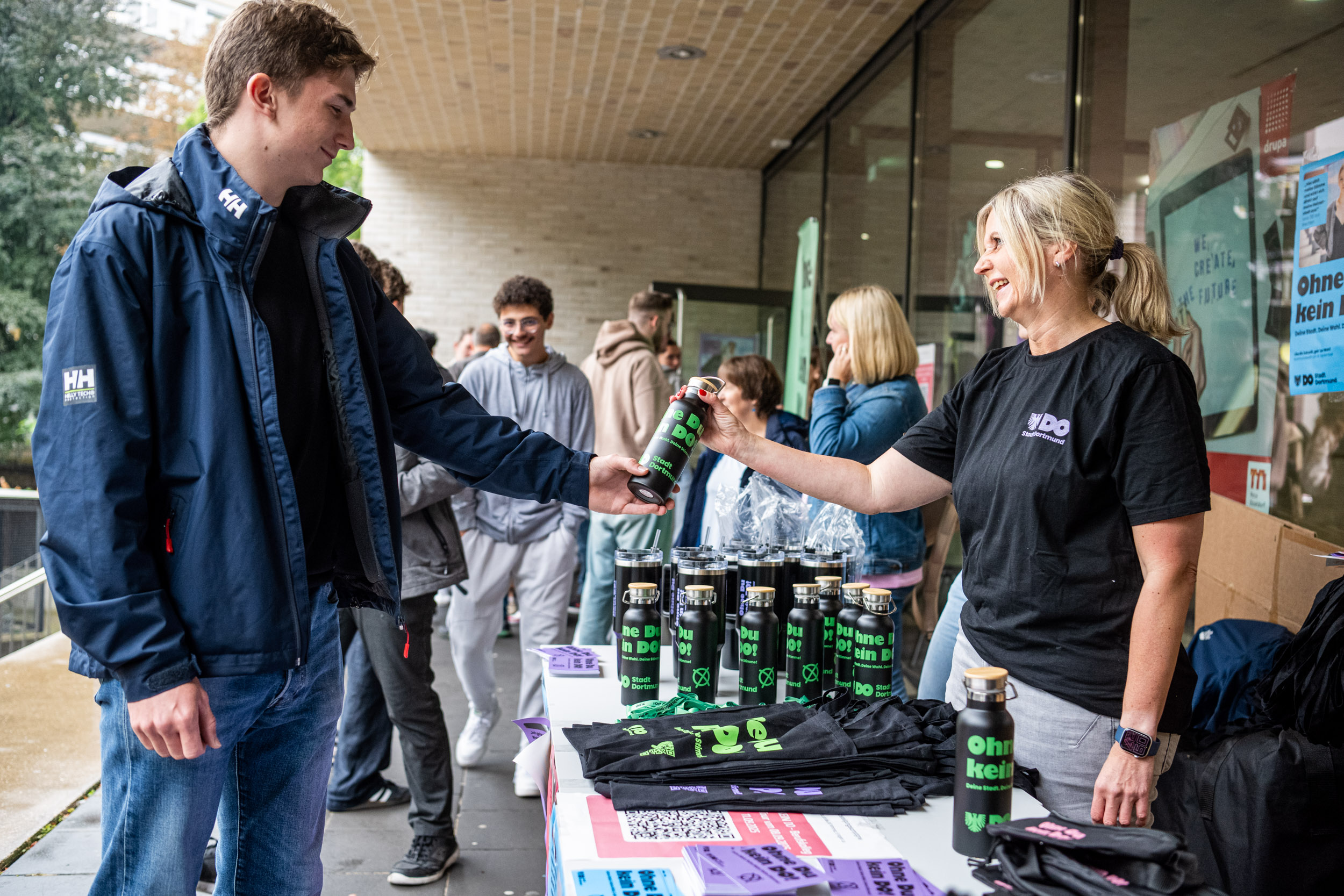 Ein Schüler vom Fritz-Henßler-Berufskolleg nimmt eine Flasche mit dem Aufdruck "Ohne du kein do" entgegen.