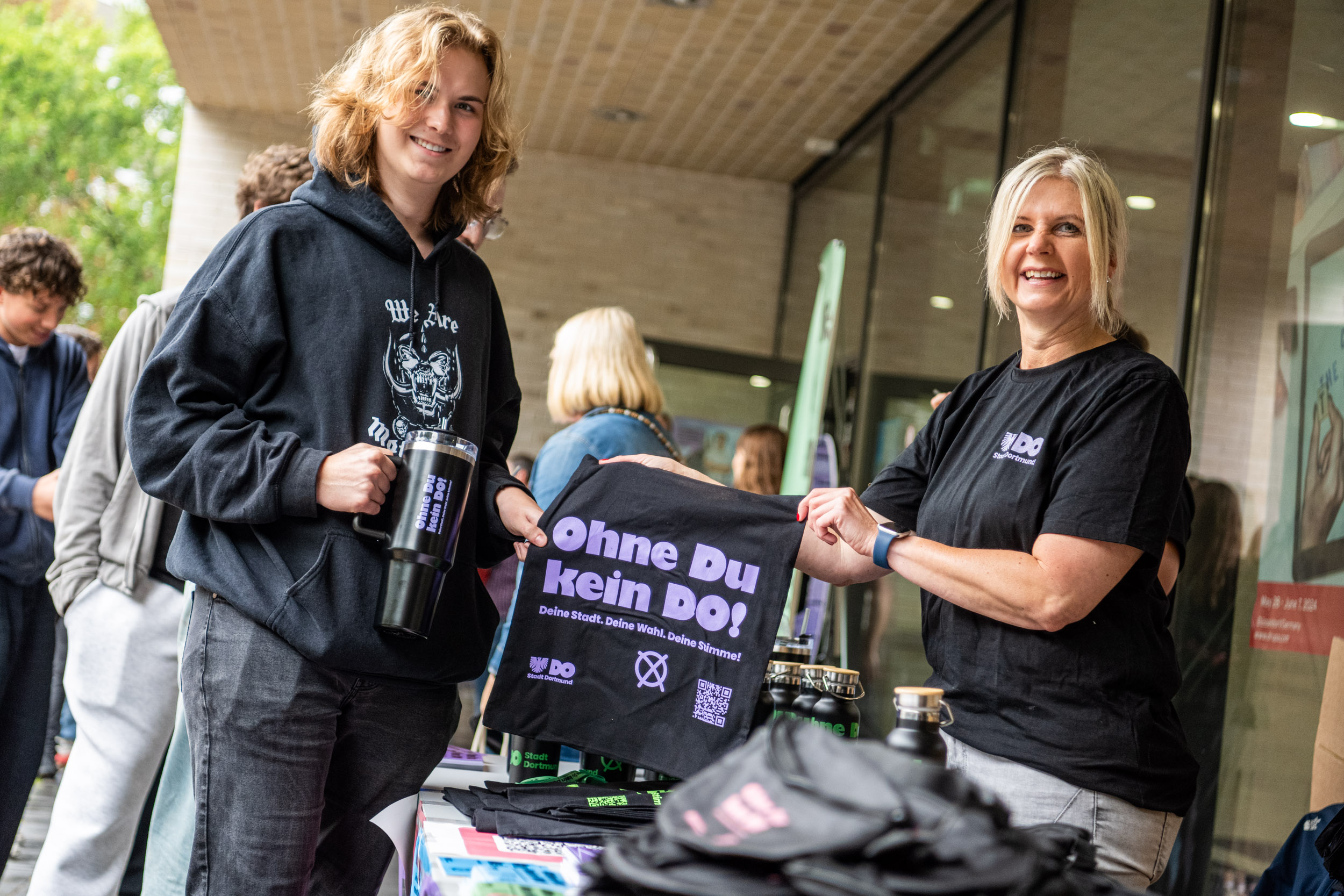 Ein Schüler und die Verantwortliche für die Wahlbeteiligungskampagne "Ohne du kein do" halten einen bedruckten Beutel hoch.