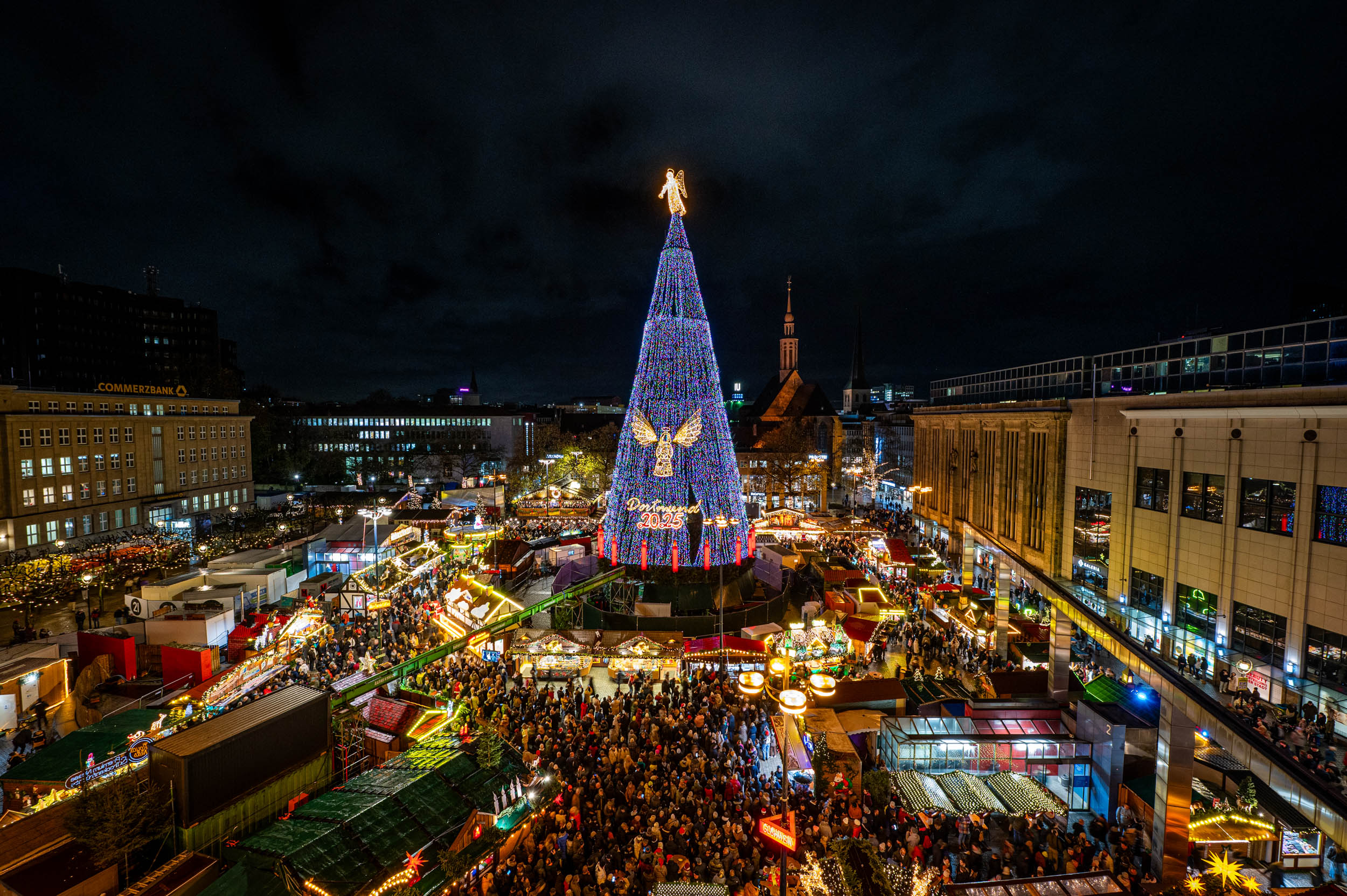 In der Totalen ist der hell erleuchtete Weihnachtsbaum 2025 auf dem Hansaplatz zu sehen. Überall leuchten die Buden feierlich.