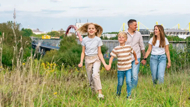 Eine Familie spaziert über eine Wiese und im Hintergrund ist die Skyline von Dortmund zu sehen