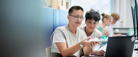 Zwei Junge Menschen halten eine Konstruktion hoch, die an einem Laptop angeschlossen ist