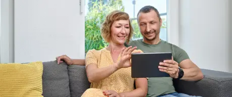 Paar sitzt auf einer Couch und sieht sich etwas auf einem Tablet an. Im Hintergrund sieht man durch ein Fenster den Florianturm.