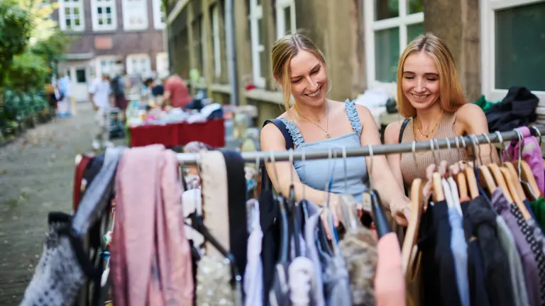 zwei Frauen schauen sich draußen an einer Kleiderstange hängende Kleidung an