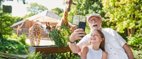 Opa und Enkelin schießen ein Selfie vor den Giraffen im Dortmunder Zoo