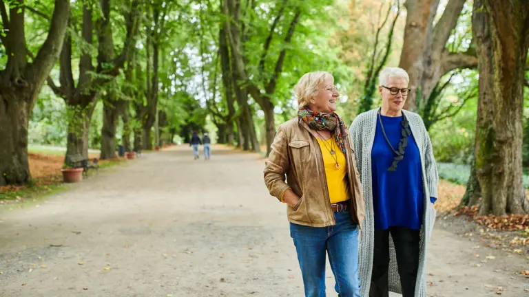 Zwei Seniorinnen spazieren lachend durch den Rombergpark