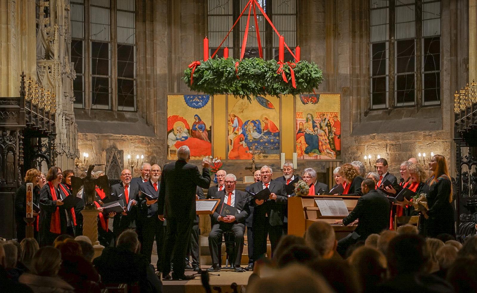 Menschen singen auf einer Bühne, darüber ein Adventskranz.