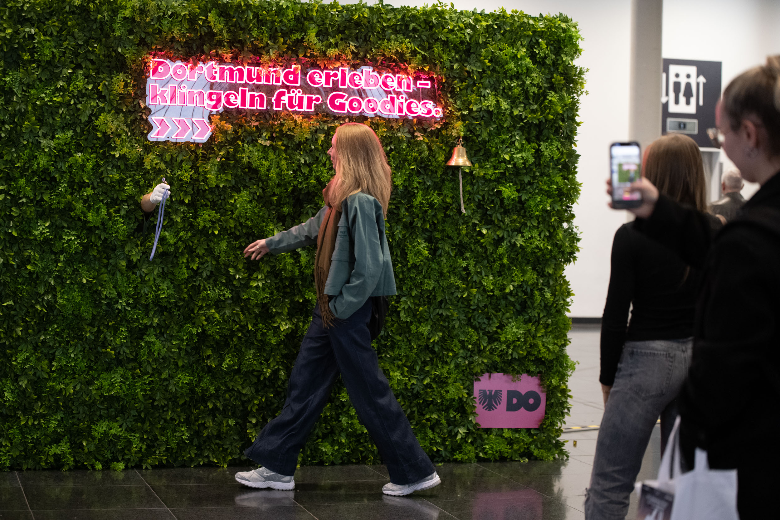 Frau steht vor einer Efeu-Wand und bekommt Goodies von einer Hand.