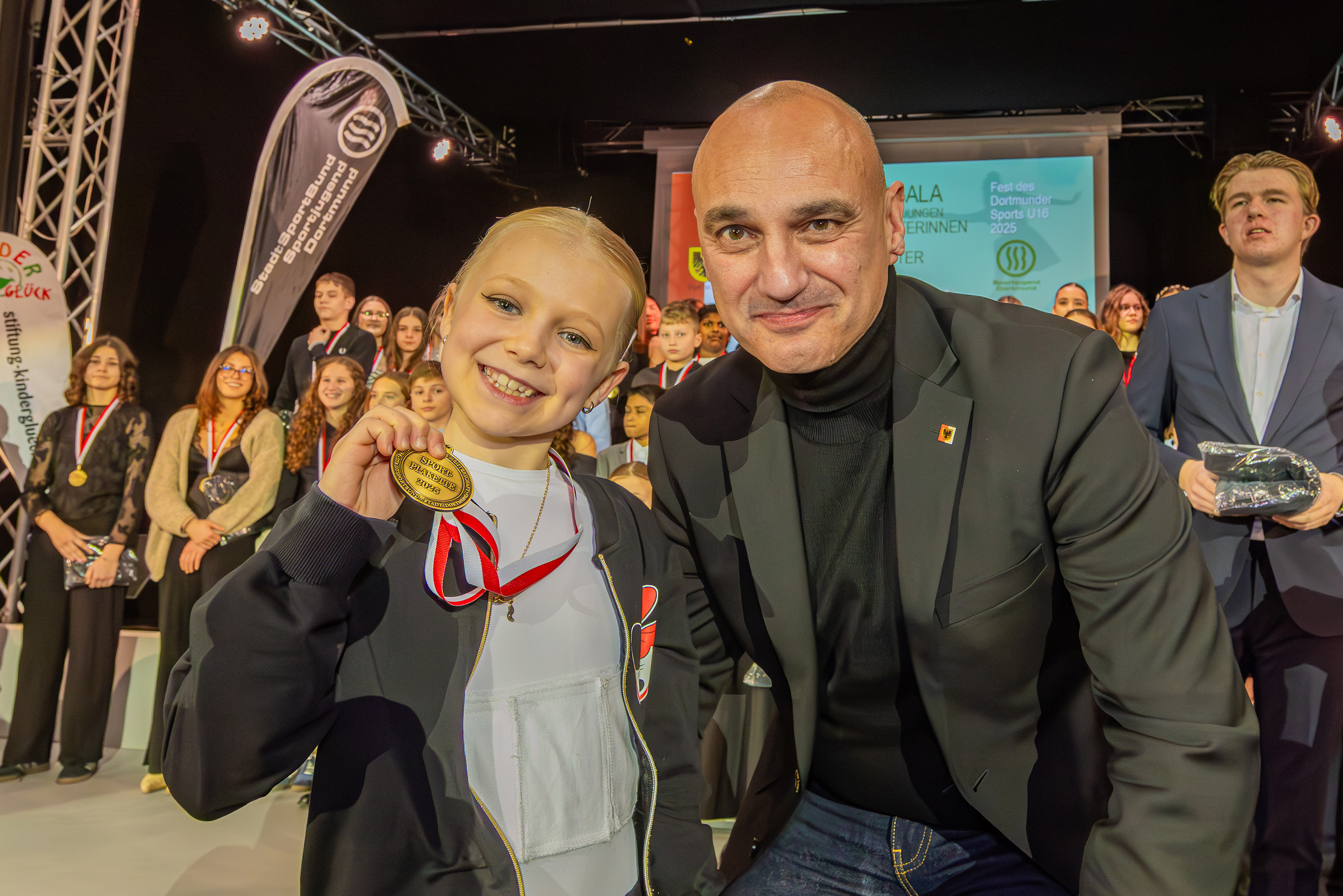 Ein Mädchen hält ihre Medaille in die Kamera, rechts daneben Oberbürgermeister Kalouti.