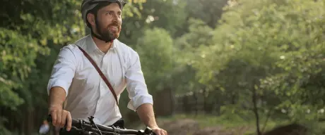 Mann mit Helm fährt mit dem Fahrrad durchs Grüne.