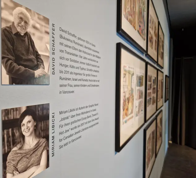 Ein Blick in die Ausstellung "Aber ich lebe" im schauraum: comic + cartoon. An der Wand hängt ein Porträtfoto des Überlebenden David Schaffer und ein Porträt der Comic-Künslterin Miriam Libicki. Im Hintergrund sind Ausschnitte aus dem Comic zu sehen, in dem es um David Schaffers Überlebensgeschichte geht.
