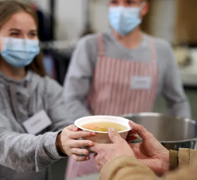 Eine Sozialarbeiterin reicht einer obdachlosen Person eine Schale Suppe