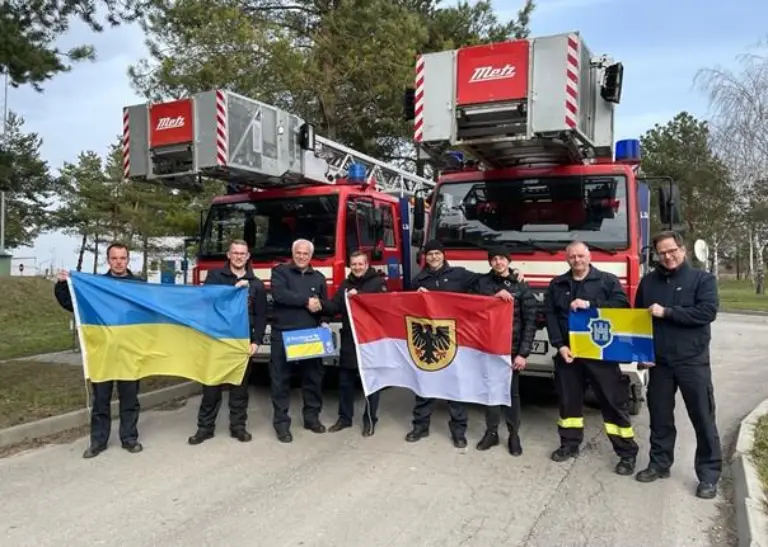 Mitarbeitende der Feuerwehr, des Rettungsdienst und des Katastrophenschutz posieren gemeinsam mit Ukraine- und Dortmund-Fahne vor zwei Drehleiterfahrzeugen