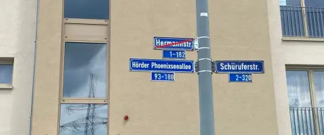 Das alten und neuen Straßenschild im öffentlichen Raum. Der alte Name ist dabei mit einem roten Strich versehen.