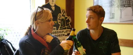 Zwei Personen sitzen an einem Tisch mit BVB-Tischdecke und prosten sich mit Bierflaschen zu.