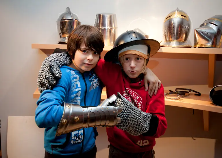 Zwei junge Besucher probieren mittelalterliche Kleidungstücke an.
