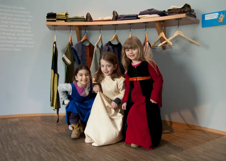 Drei Mädchen probieren mittelalterliche Kleidungsstücke an.