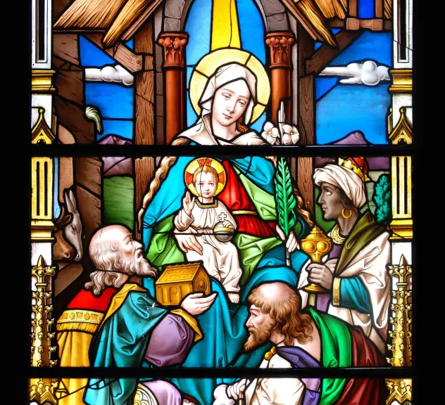Bunt bemaltes Kirchenglasfenster, im Zentrum eine Frau mit Baby auf dem Schoß und drei Könige, die davor knien.