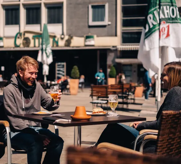 Zwei Personen sitzen an einem Tisch auf dem alten Markt unterhalten sich und trinken etwas.