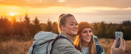 Zwei Frauen mit Wanderrucksäcken machen ein Selfie von sich.