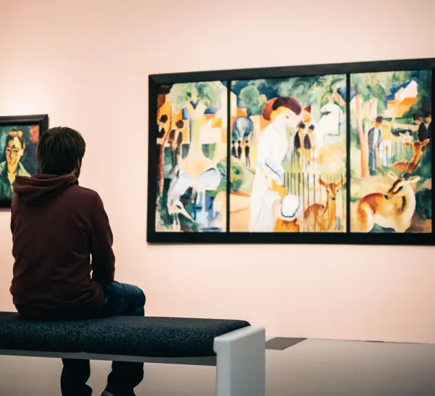 Ein Mann sitzt im Museum auf einer Bank und schaut sich ein Gemälde an.