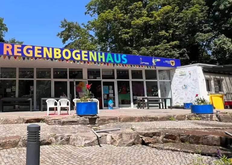 Besucher*innen vor dem Regenbogenhaus im Westfalenpark an einem sonnigen Tag, die lebendige Farbgestaltung des Gebäudes unterstreicht den einladenden Charakter des Ortes