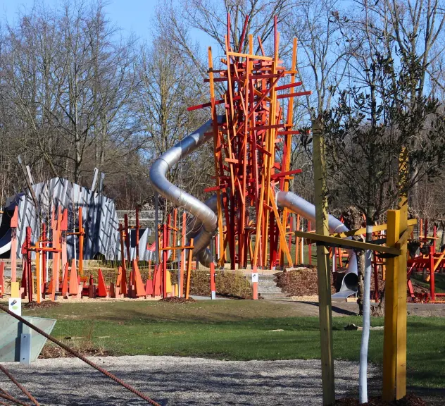 Innovativer Robinson-Spielplatz im Westfalenpark mit Rutschen und Kletterstrukturen in Orange und Grau an einem klaren Tag.