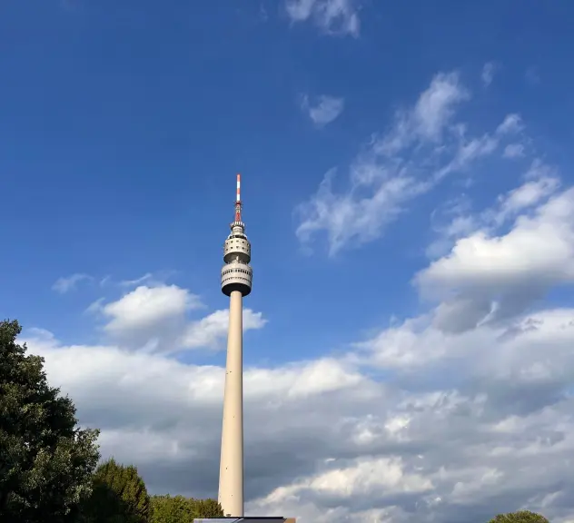 Der Florianturm im Westfalenpark Dortmund, eingefangen gegen einen dynamischen Himmel mit Wolken, bietet ein markantes Bild des modernen Dortmund, umrahmt von der natürlichen Schönheit des Parks.