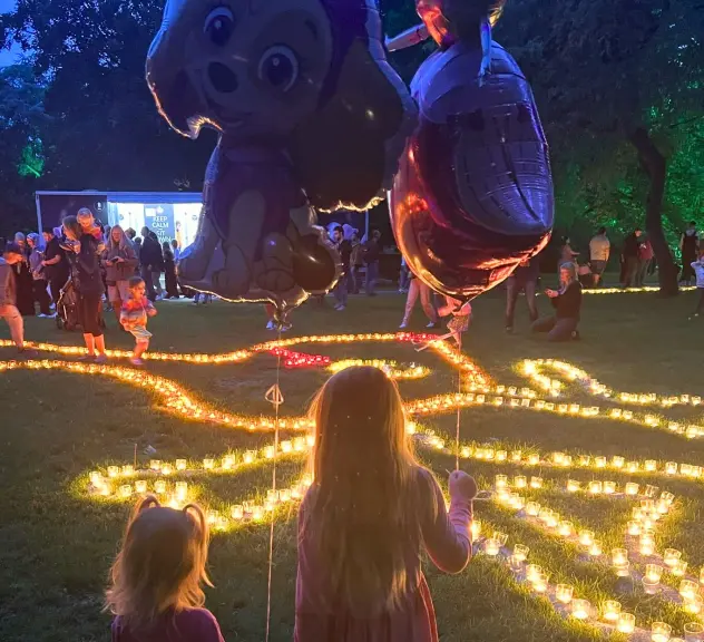 Kinder beobachten beleuchtete Wegführung beim Lichterfest im Westfalenpark, mit Luftballons und Kerzenlicht in der Dämmerung