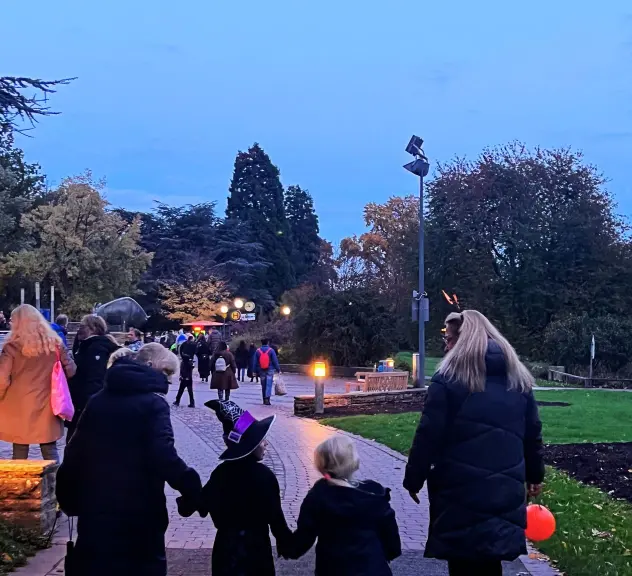 Familien beim Spaziergang durch den Westfalenpark während des Halloween-Festes bei Einbruch der Dämmerung, mit leuchtenden Laternen und kinderfreundlicher Atmosphäre