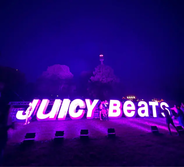 Leuchtendes Juicy Beats Festival-Logo im Westfalenpark bei Nacht mit dem Dortmunder Fernsehturm im Hintergrund