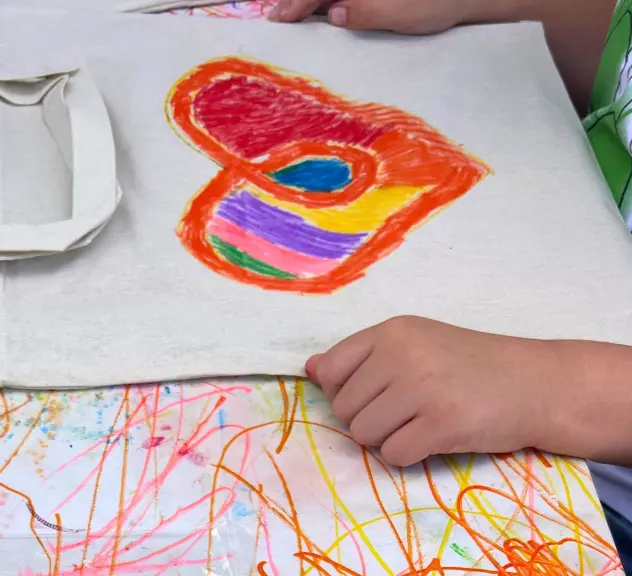 Kind malt ein buntes Herz auf Stoff beim Kreativworkshop am Weltkindertag im Regenbogenhaus, Westfalenpark