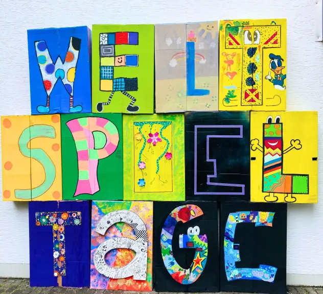 Buntes Kunstwerk zum Weltspieltag am Regenbogenhaus im Westfalenpark mit kreativ gestalteten Buchstaben, die das Wort "WELTSPIELTAGE" bilden