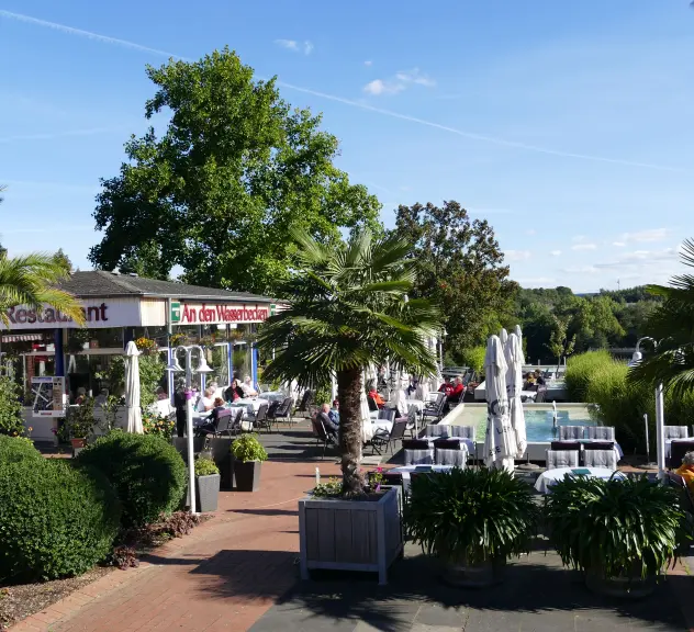 Das Café-Restaurant 'An den Wasserbecken' im Westfalenpark Dortmund, umgeben von Palmen und einer sommerlich gedeckten Terrasse