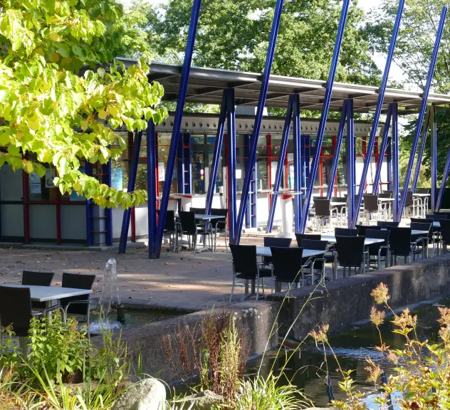 Das Zimt&Zucker im Westfalenpark Dortmund, einladend mit Außensitzplätzen nahe dem Wasser und umgeben von grüner Natur.