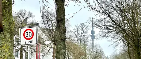 Aufnahme eines Tempo-30-Verkehrsschildes. Im Hintergrund Häuser, Bäume und der Florianturm.
