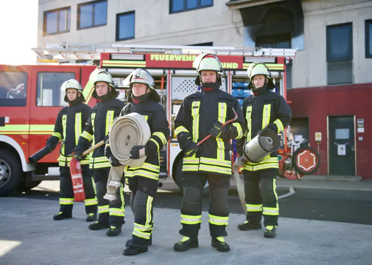 Fünf Personen in Feuerwehruniform stehen nebeneinander vor einem Feuerwehrwagen
