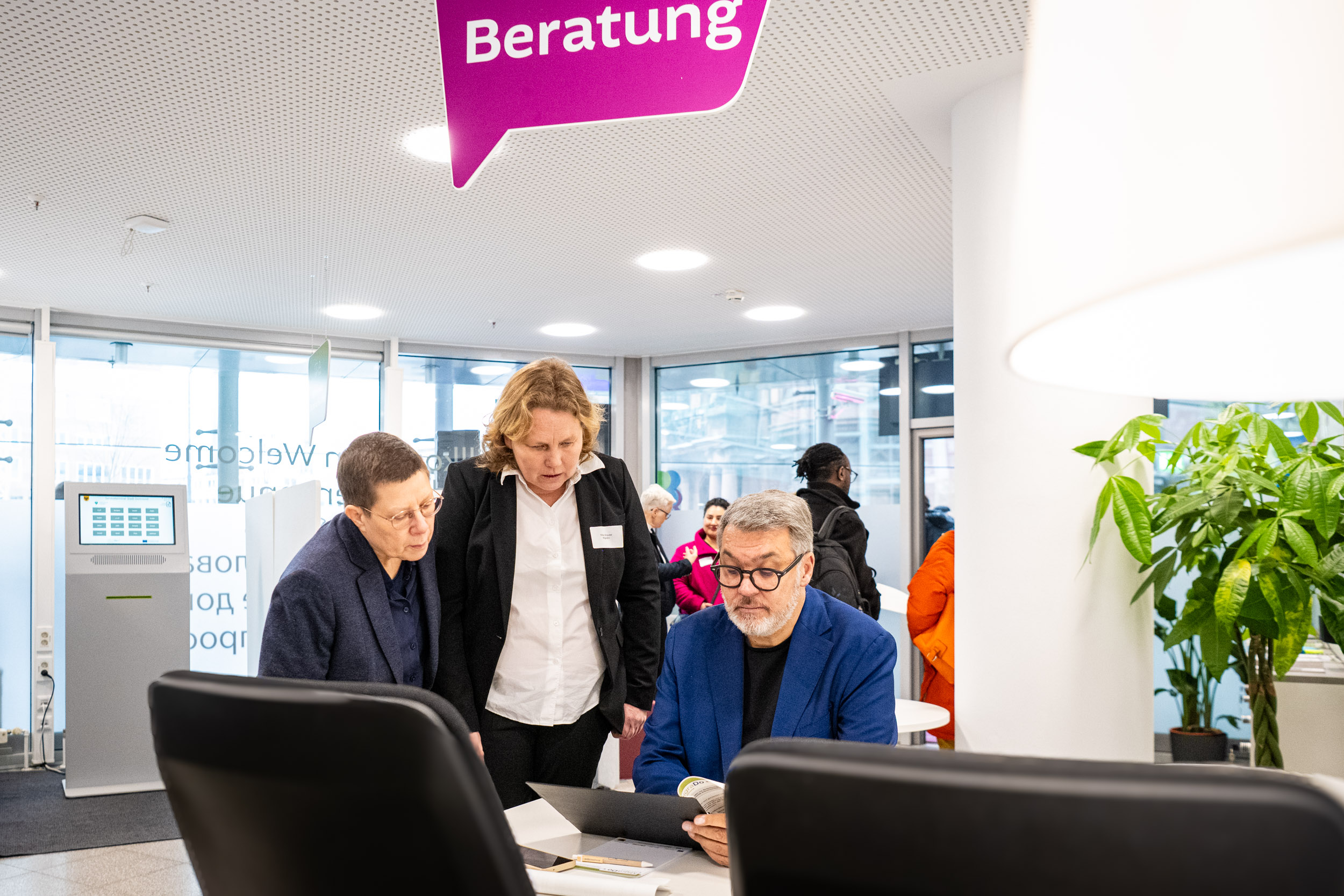 Drei Personen an einem Beratungsschalter, die auf einen Laptop schauen. 