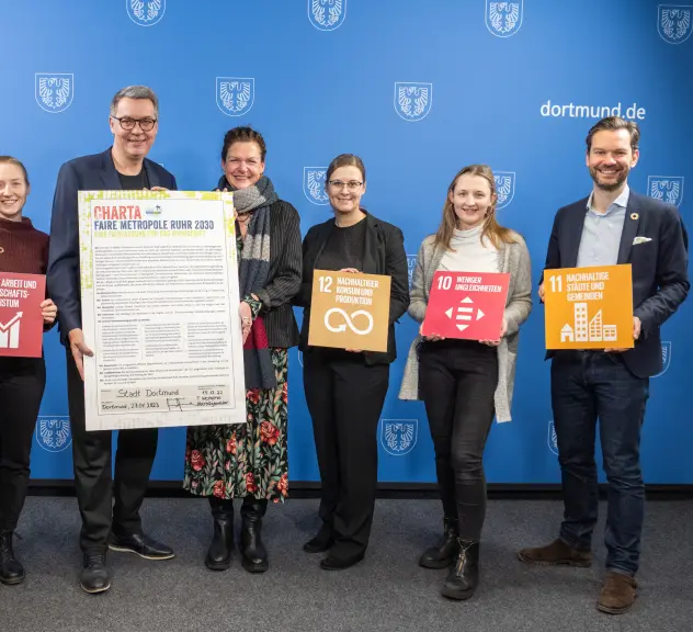 Eine Gruppe von Menschen aus Verwaltung und Zivilgesellschaft posieren mit den UN-Nachhaltigkeitszielen und der unterschriebenen Charta Faire Metropole Ruhr 2030. 