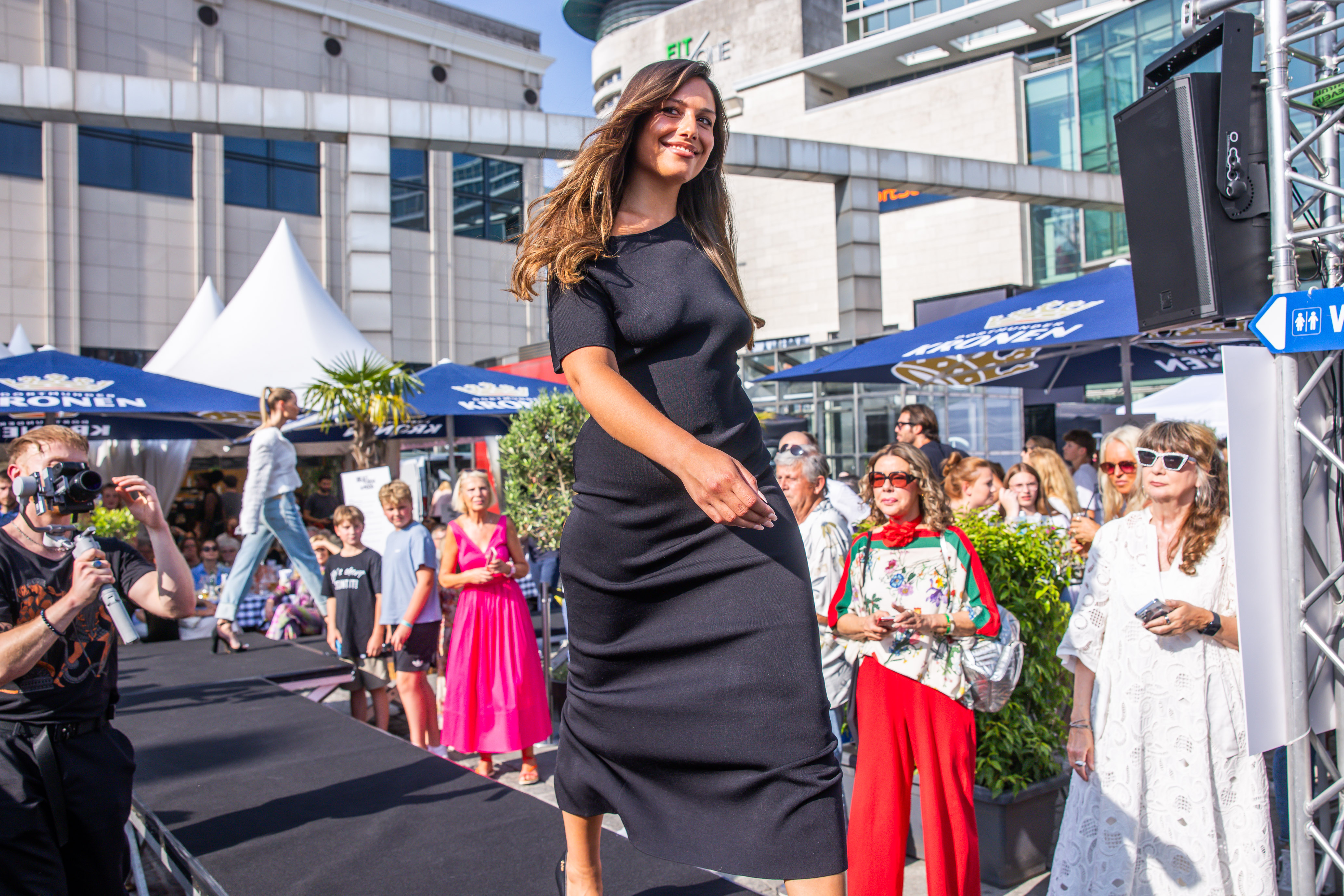 Foto einer Frau, die auf einem Laufsteg unter freiem Himmel Mode präsentiert. 
