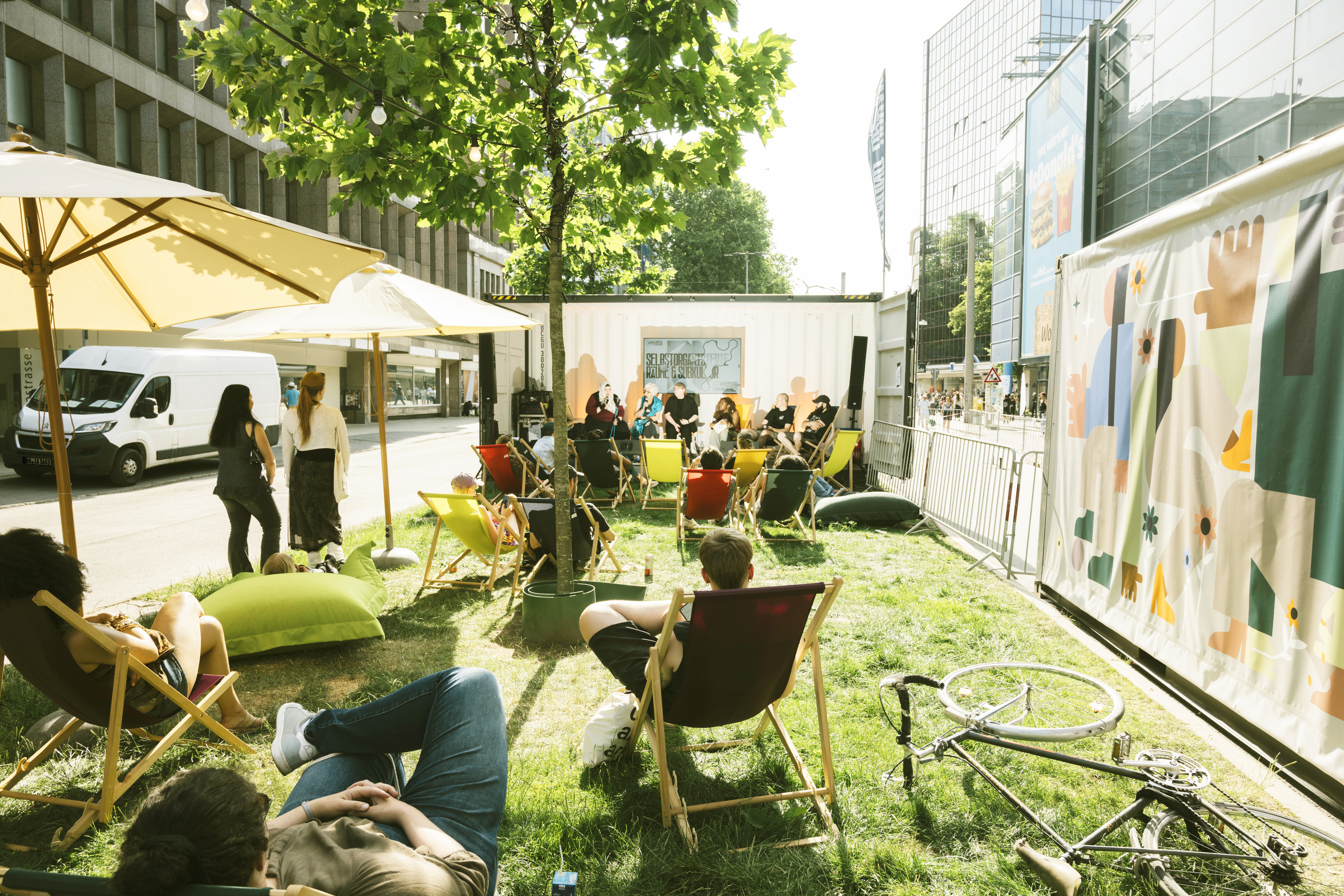 Junge Menschen in Liegestühlen auf einem Grünstreifen einer Straße. 