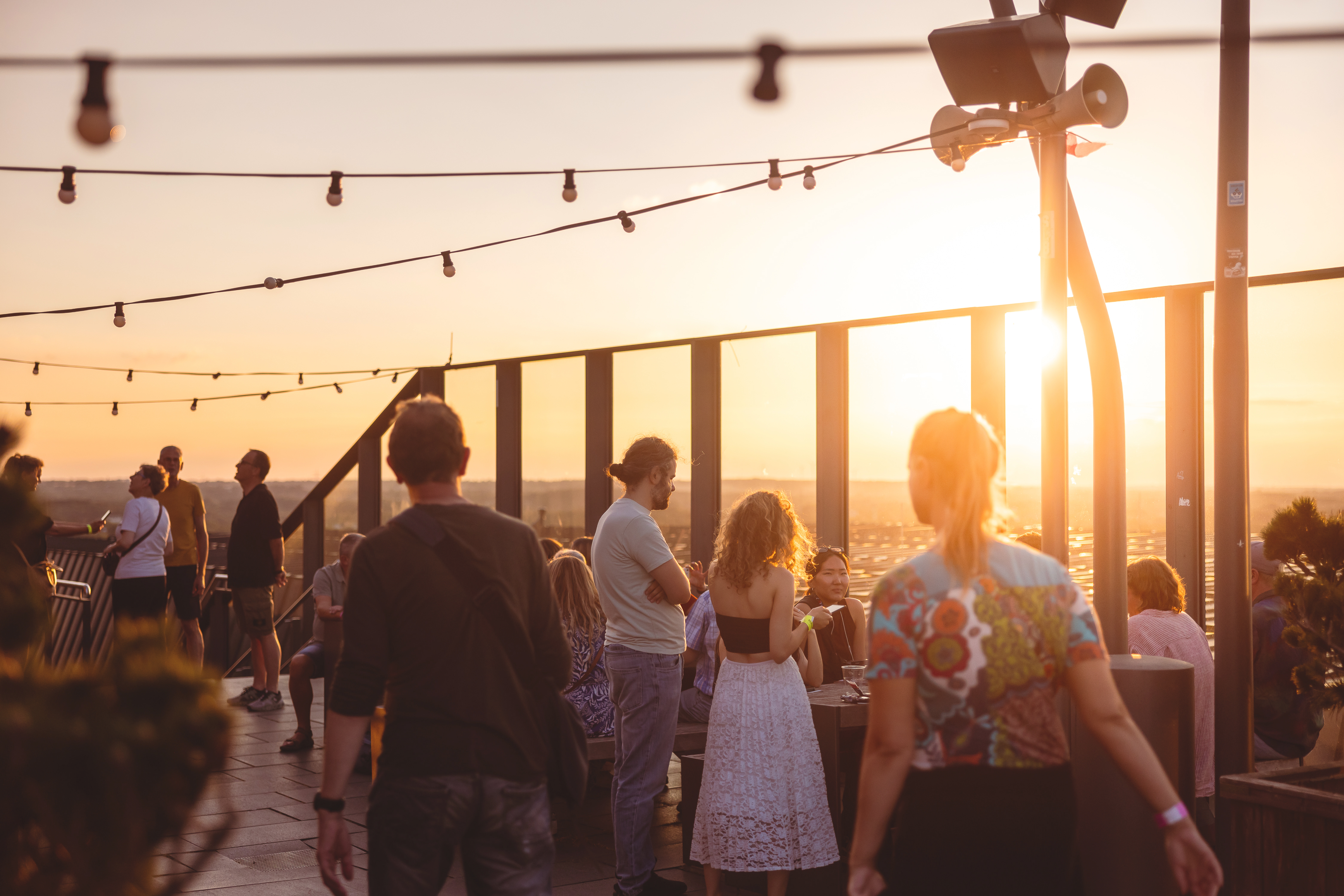 Junge Menschen auf einer hohen Dachterrasse in Sonnenuntergangsstimmung.