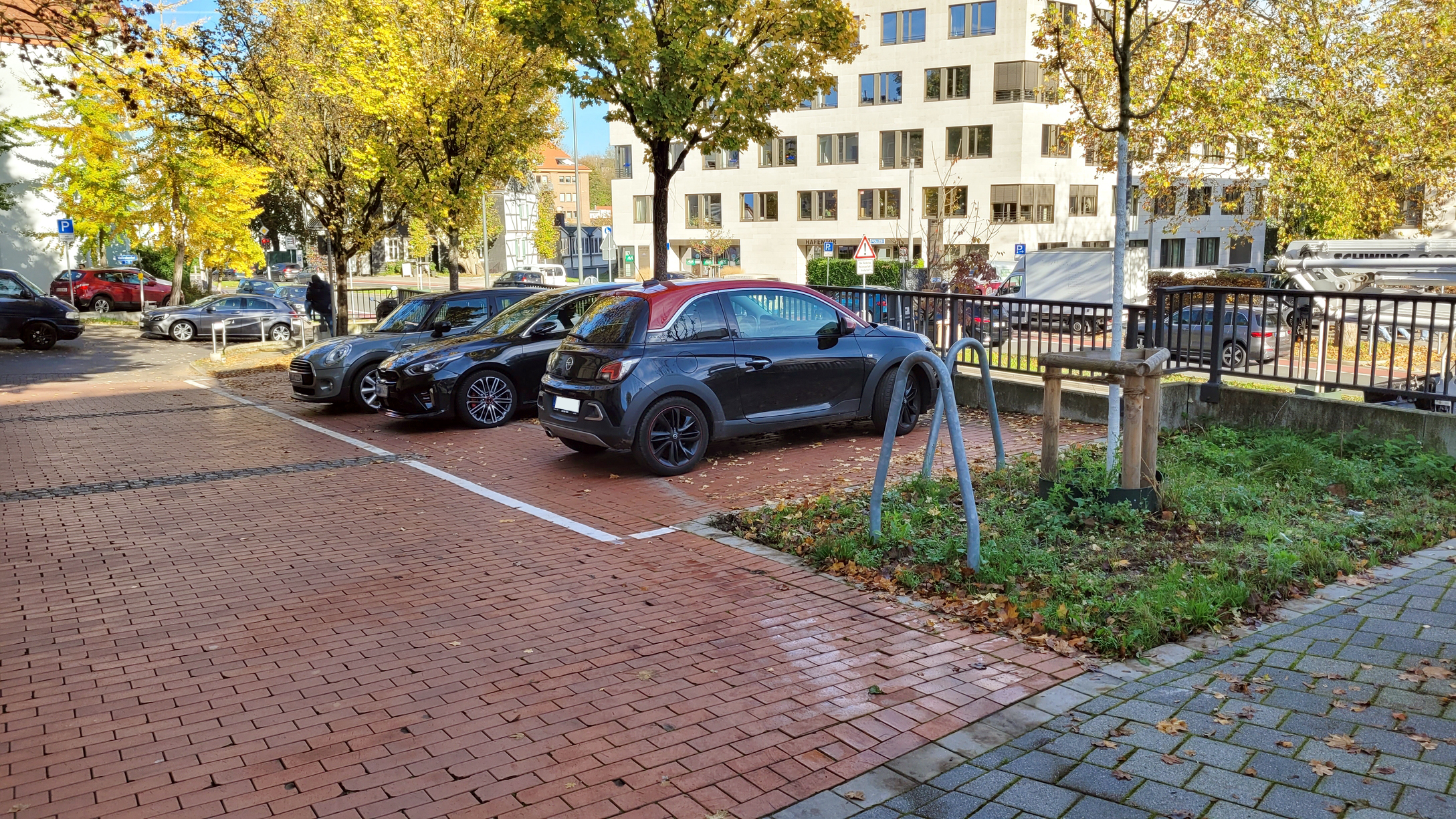 Foto parkender Autos auf einer rot gepflasterten Fläche mit markierten Parkzonen.